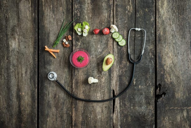 Importance of healthy eating for overall health - various fresh vegetables and medical stethoscope placed over rustic wooden background to form a smiling face.